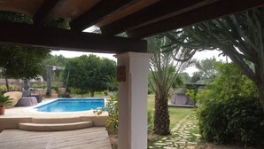 Un espacio al aire libre techado con piscina, terraza de madera y vegetación circundante.