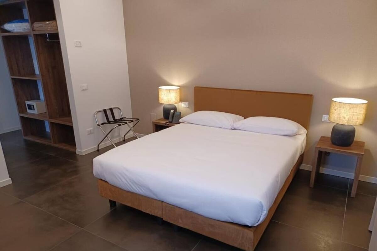 A neatly made bed with white linens, two bedside lamps, and a wooden headboard.