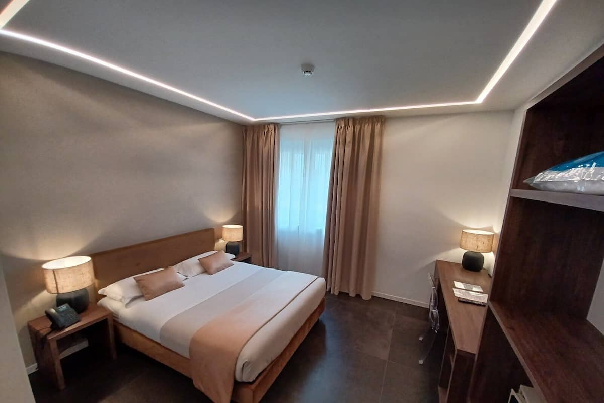 A modern hotel room with a large bed, bedside lamps, a desk, and a television.