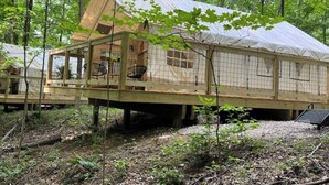 Une cabane en bois dotée d’un balcon en verre, entourée d’arbres.