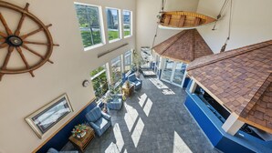 A high-ceilinged room with a large wooden wheel, a hanging chair, and a view of the outdoors through large windows. - Bayshore Resort (Put-in-Bay)