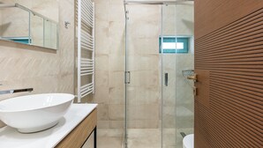 Ein modernes Badezimmer mit einem großen, weißen Waschbecken, einer Duschkabine aus Glas und einer Holzpaneelausstattung.