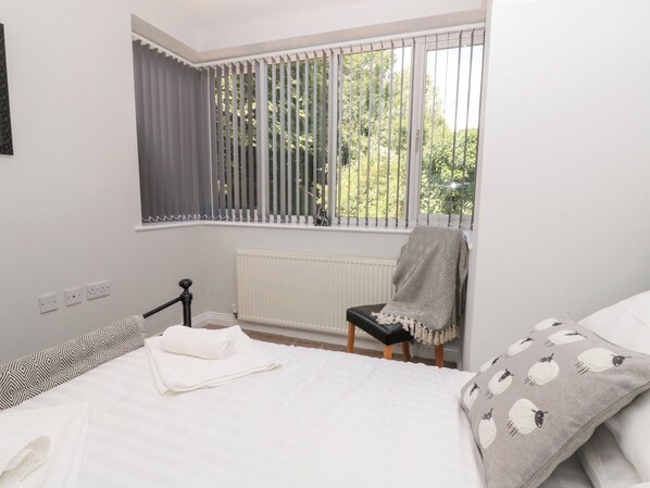 A bedroom with a bed, a chair, a radiator, and a window with blinds.