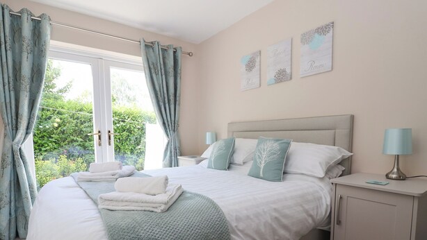 A bedroom with a bed, bedside tables, a nightstand, and a view of greenery outside. - Church View (Hull)