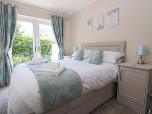 A bedroom with a bed, bedside tables, a nightstand, and a view of greenery outside.