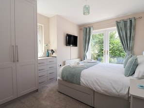 A bedroom with a bed, a dresser, a TV, and a window with curtains.