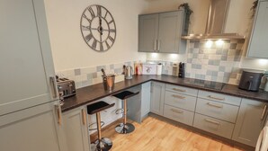 A modern kitchen with grey cabinets, a stainless steel range hood, a clock, and a bar stool. - Church View (Hull)