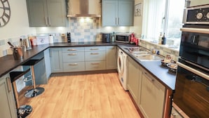 A modern kitchen with grey cabinets, a stainless steel range hood, a built-in dishwasher, and a double oven. - Church View (Hull)