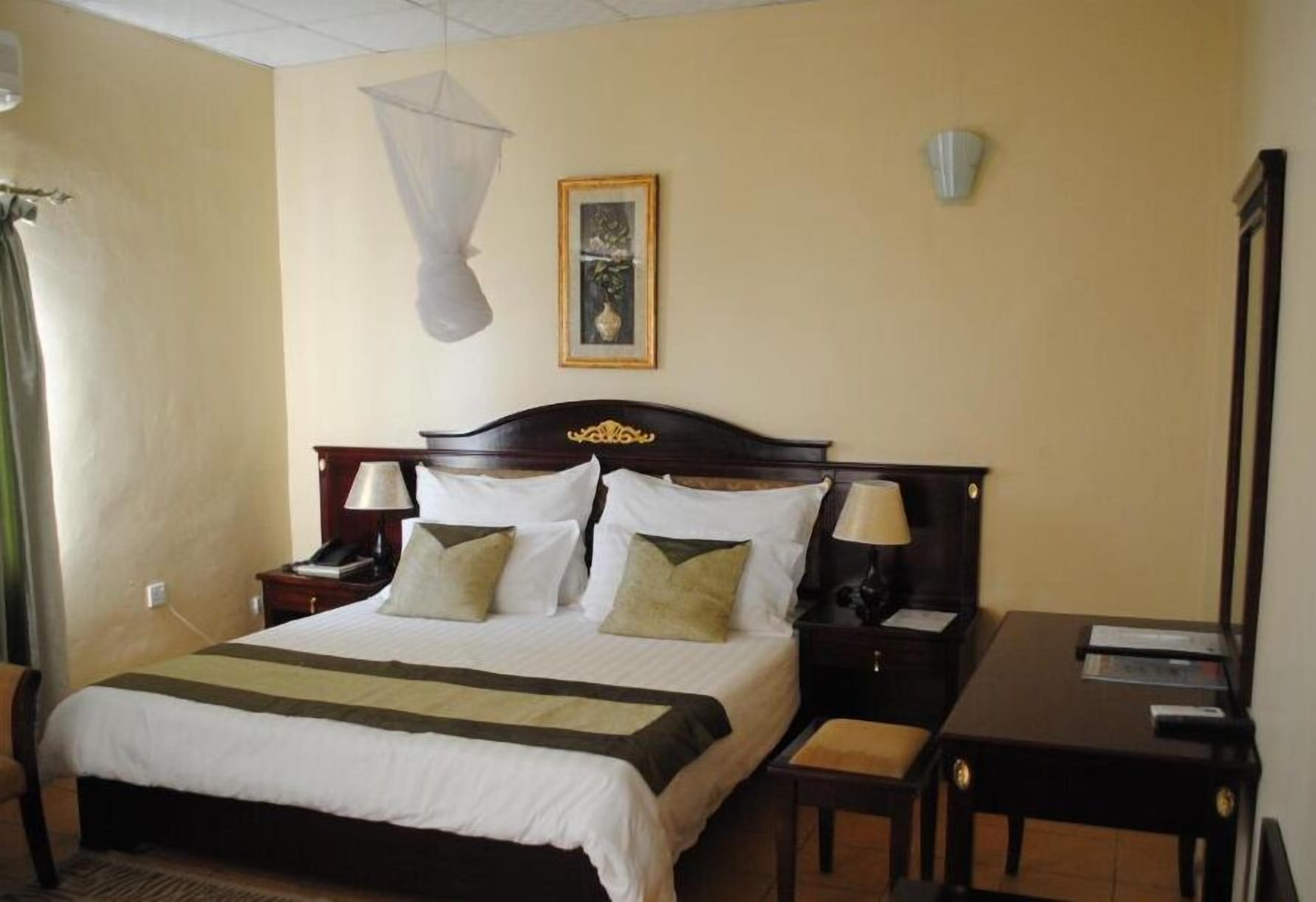 A hotel room with a bed, bedside tables, a desk, a chair, and a picture on the wall.
