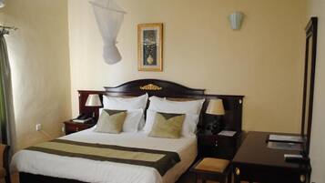 A hotel room with a bed, bedside tables, a desk, a chair, and a picture on the wall.