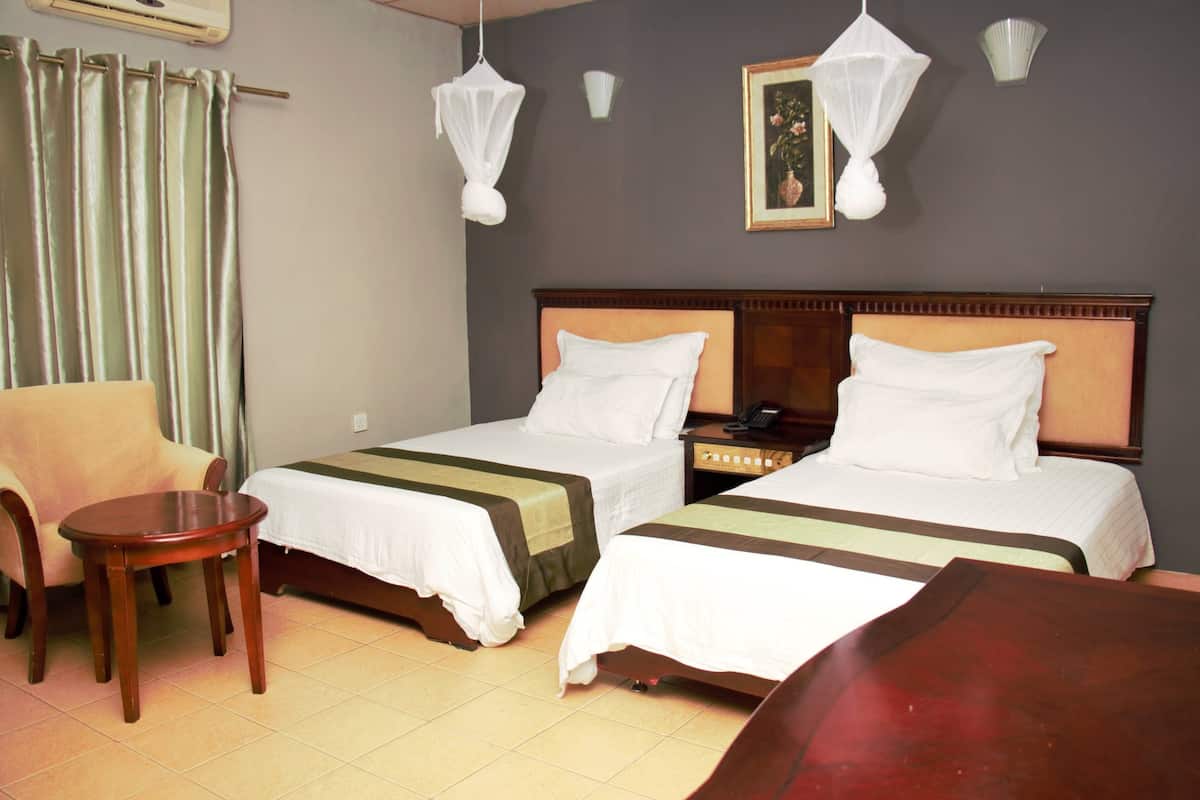 A hotel room with two beds, a chair, a small table, and a nightstand with a lamp.