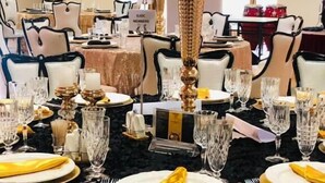 A formal dining room with tables set for a banquet, featuring gold and black tablecloths, white chairs, and a large floral centerpiece. - Moba Hotel & Convention Centre (Kitwe)