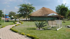 A paved pathway, a thatched-roof structure, and a seating area with chairs and an umbrella. - Moba Hotel & Convention Centre (Kitwe)