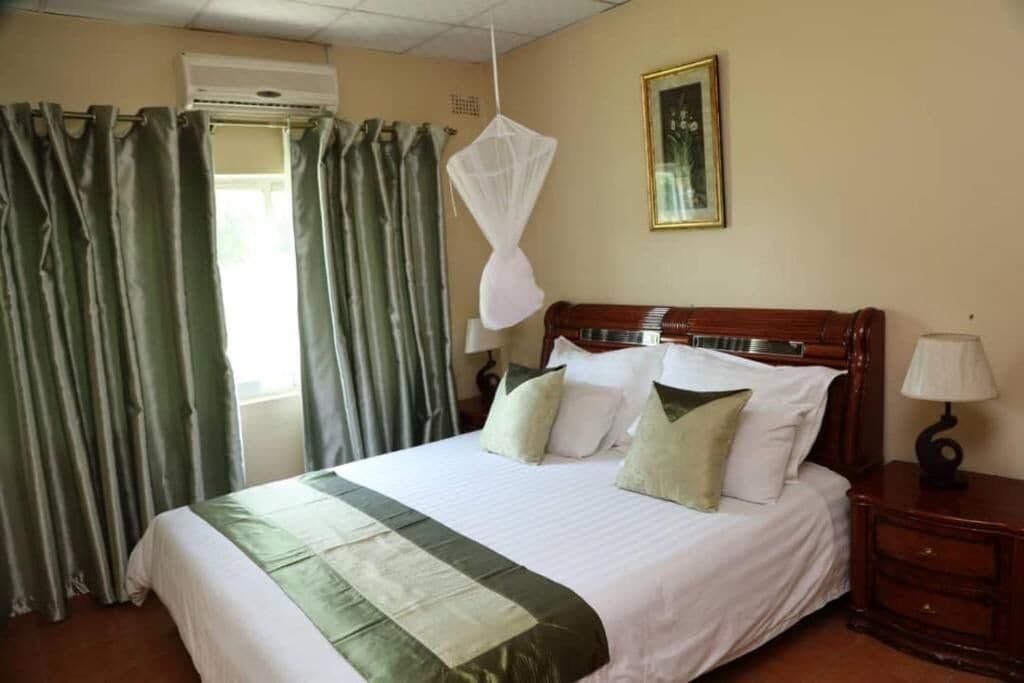 A neatly made bed with a green and white bedspread, a wooden headboard, and a bedside table with a lamp.