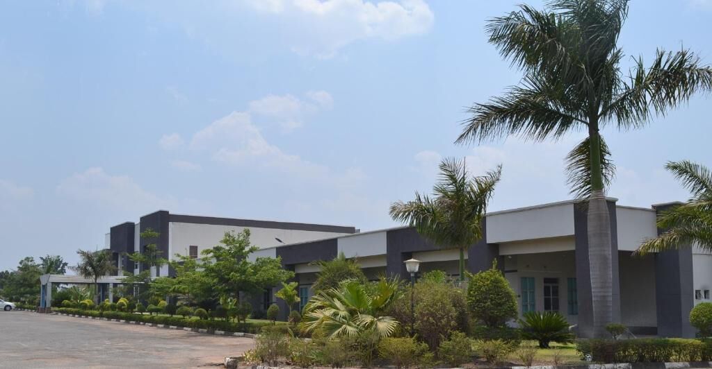 A modern building with a flat roof, surrounded by well-maintained greenery and palm trees.