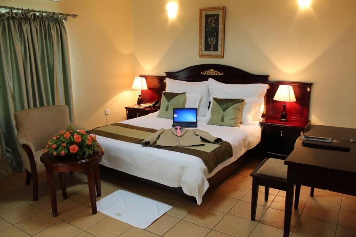 A hotel room with a bed, two bedside tables with lamps, a chair, a small table with a flower arrangement, and a laptop on the bed.