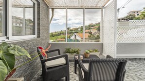 A balcony with wicker furniture, a view of a town, and a white lattice fence. - Upland Home I by Madeira Sun Travel (Ponta do Sol)
