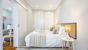 A modern hotel room with a large bed, a bedside table with a lamp, and a view of a cityscape through the window. - Upland Home I by Madeira Sun Travel (Ponta do Sol)