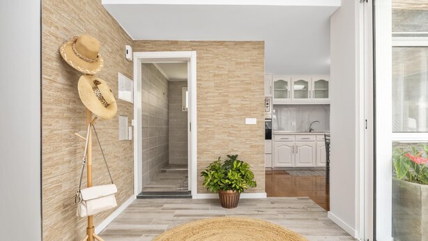 A modern interior with a hallway leading to a kitchen, featuring a wooden wall, a potted plant, and a straw hat on a stand. - Upland Home I by Madeira Sun Travel (Ponta do Sol)