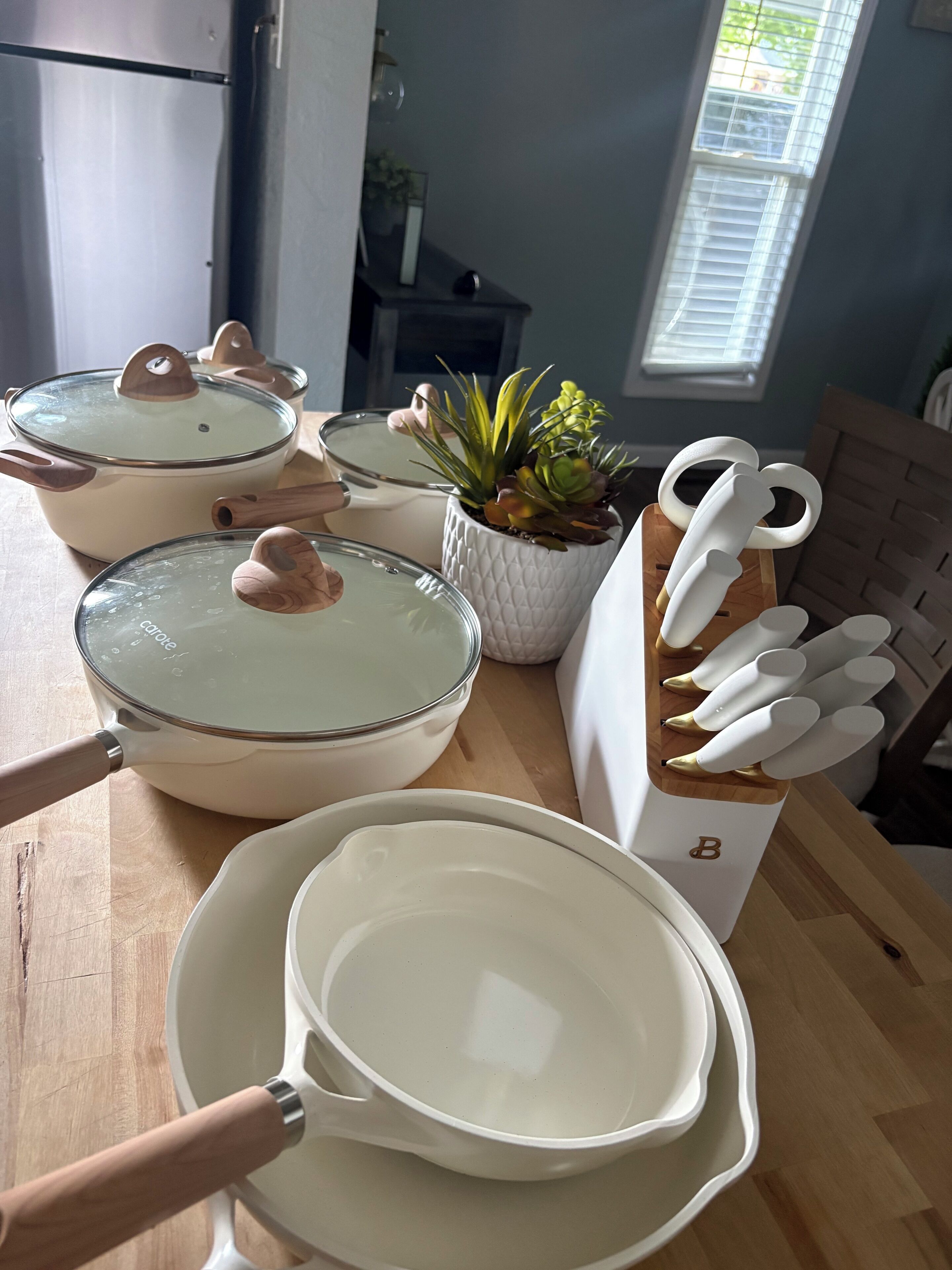 Una cocina con utensilios de cocina blancos, incluyendo ollas y sartenes, y un juego de cuchillos sobre un bloque de madera.