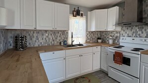 A kitchen with white cabinets, a wooden countertop, a stove, and a window with a curtain. - Cheerful Bronson Cutie
 (Bronson)