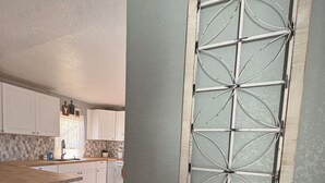A kitchen with white cabinets, a wooden countertop, and a decorative window with a geometric design. - Cheerful Bronson Cutie
 (Bronson)