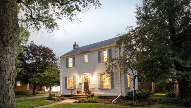 A two-story house with a front porch, a well-maintained lawn, and a tree in the foreground. - Charming Old Orchard home with fenced yard (Toledo)