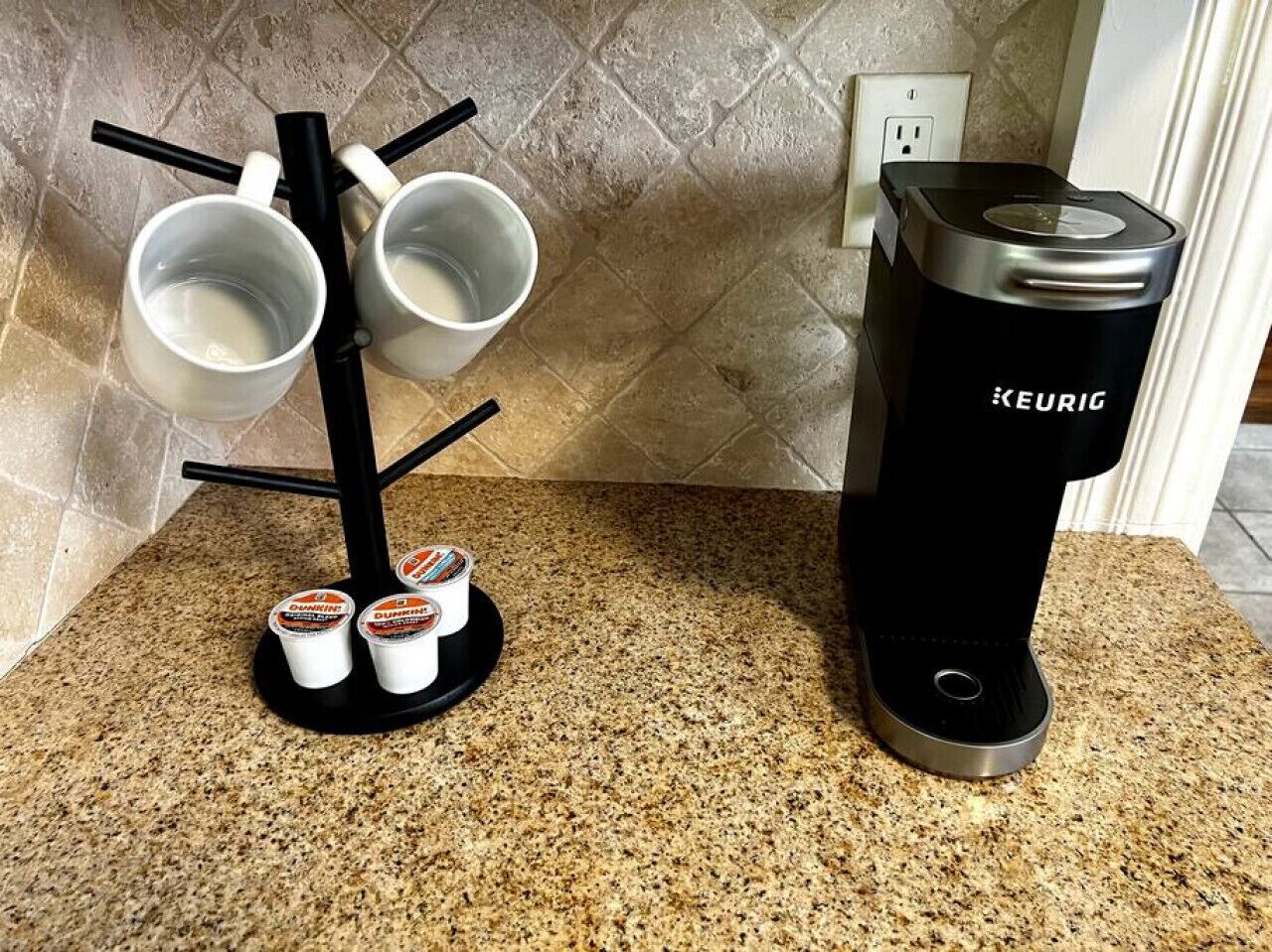 A kitchen with a coffee maker, a mug rack, and two cups of yogurt.