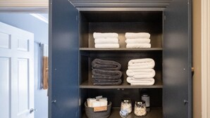 A storage cabinet with shelves holding folded towels and containers with bath products. - Charming Old Orchard home with fenced yard (Toledo)