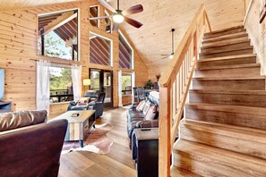 Un vaste espace de vie agrémenté d’un escalier en bois, de grandes fenêtres et d’un ventilateur de plafond.