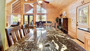 A spacious wooden cabin with a large dining table, a ceiling fan, and a view of the outdoors. - Modern & Private Cabin Retreat Near Sitgreaves National Forest! (Overgaard)