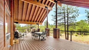 A wooden deck with a table and chairs, a covered area with a roof, and a view of trees and landscape. - Modern & Private Cabin Retreat Near Sitgreaves National Forest! (Overgaard)