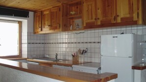 A kitchen with wooden cabinets, a tiled backsplash, a white refrigerator, and a wooden countertop.