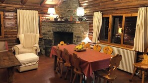 A cozy dining area with a stone fireplace, wooden chairs, a table with a red tablecloth, and a chandelier.