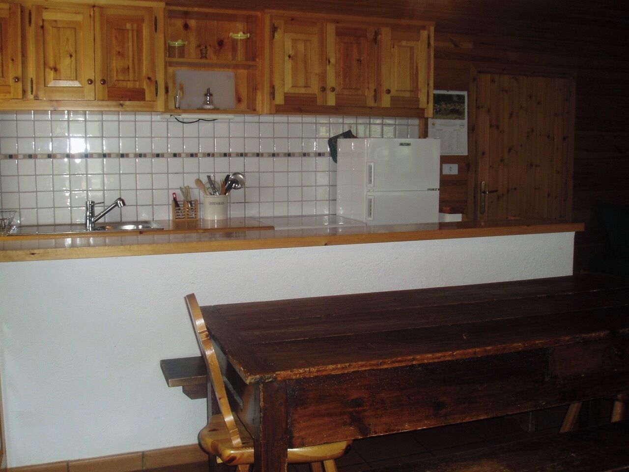 A kitchen with wooden cabinets, a white tiled backsplash, a white refrigerator, and a wooden bench.