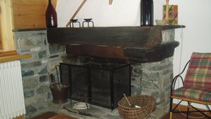 A stone fireplace with a wooden mantel, a woven basket, and a plaid chair.