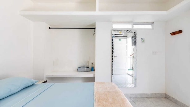 A minimalist bedroom with a bed, a small shelf, and a door leading to a balcony. - alborada hostel B&B  (Santa Marta)