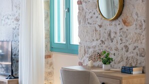 Ein Zimmer mit Steinwand, einem Holztisch mit Spiegel, einer Topfpflanze und einem Fenster mit blauen Fensterläden.