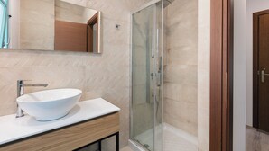Ein modernes Badezimmer mit einem großen, weißen Waschtisch, einer Duschkabine aus Glas und einem Holzwaschbeckenunterschrank.