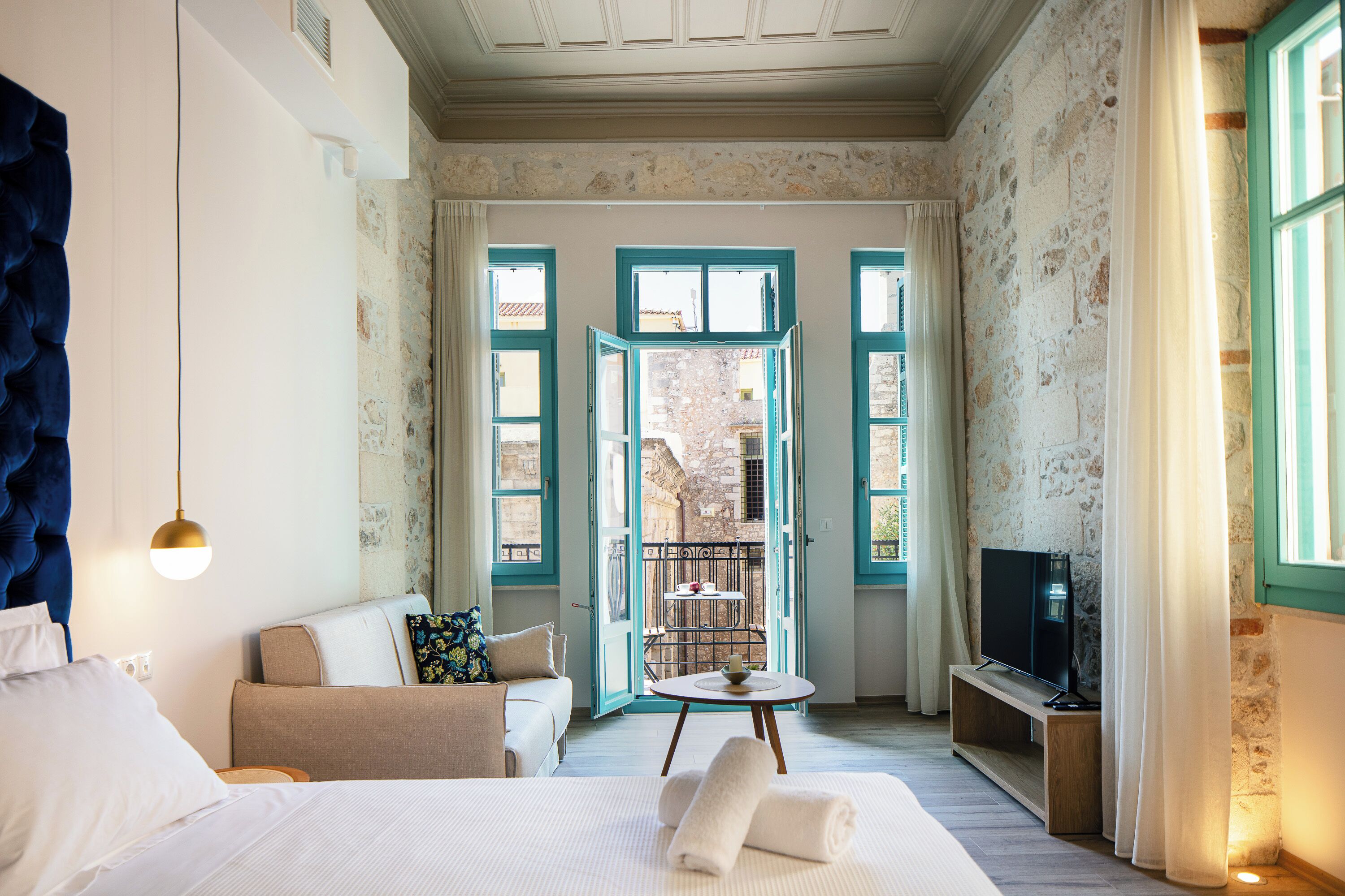 A hotel room with a bed, a sofa, a TV, and a balcony with a view.
