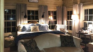 A cozy bedroom with a wooden ceiling, a large bed with multiple pillows, a chair, and a table with a lamp. - Romantic Secret Cottage near downtown Carthage (Carthage)