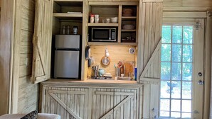 A rustic kitchen with wooden cabinets, a refrigerator, a microwave, and a window with a view of trees. - Romantic Secret Cottage near downtown Carthage (Carthage)