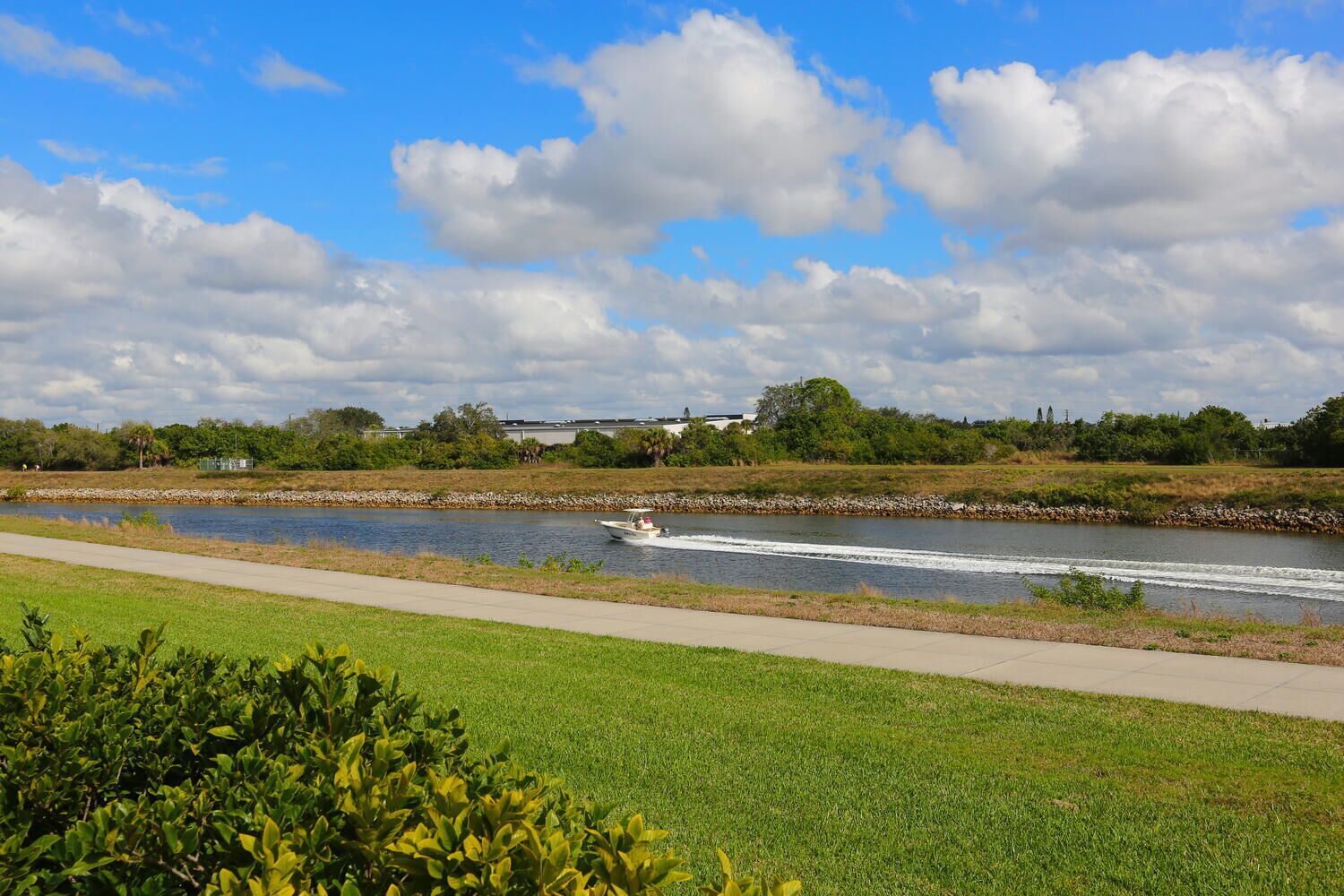 A river with a boat, a paved walkway, and greenery.