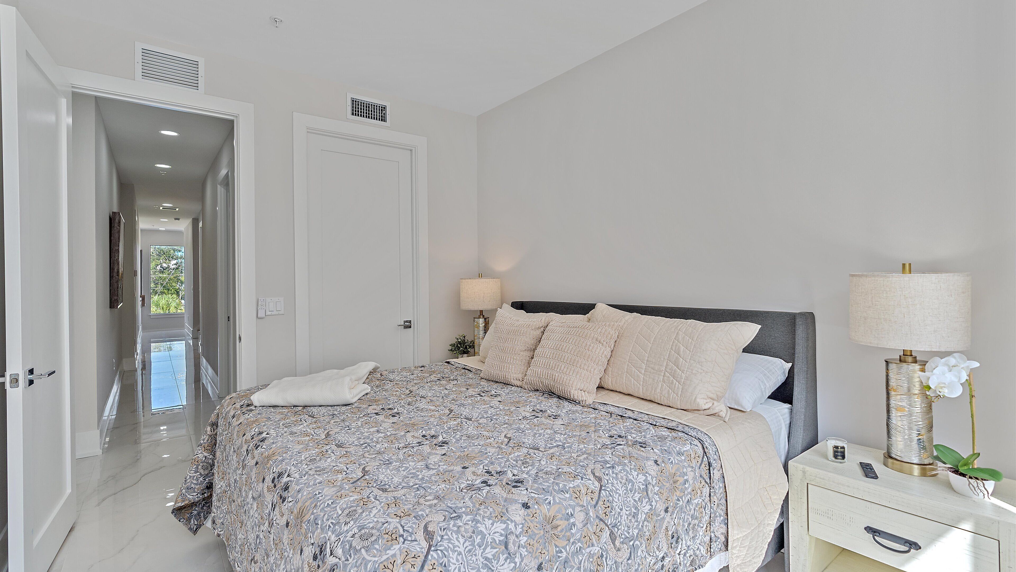 A bedroom with a bed, bedside table, lamp, and a view of the outdoors.