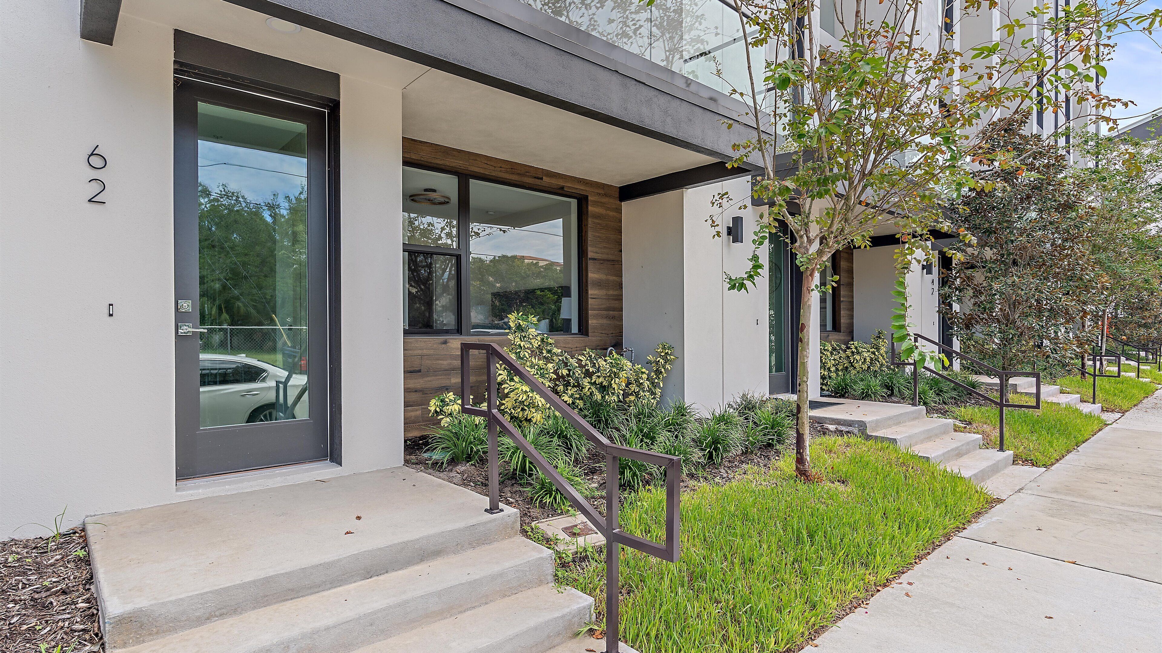 A modern building with a glass door, a staircase with metal railings, and a well-maintained lawn.