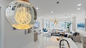 Un interno moderno con un lampadario sferico, un'area pranzo e un soggiorno con divano e televisore.