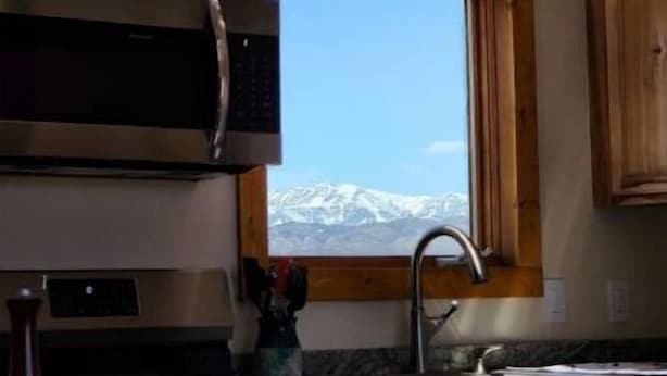 A kitchen with wooden cabinets, a stainless steel microwave, and a window with a view of snow-capped mountains. - The Bunk House (Cody)