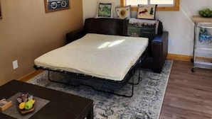 A bedroom with a loft bed, a small table with fruit, a radiator, and a window with blinds. - The Bunk House (Cody)