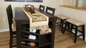 A dining area with a table set for four, a wine rack below, and a large black and white road painting on the wall. - Easy Living ~ Easy Playing, just a 5 minute walk from down town Cody. (Cody)