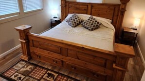 A bedroom with a wooden bed, two bedside tables, and a window with blinds. - Easy Living ~ Easy Playing, just a 5 minute walk from down town Cody. (Cody)